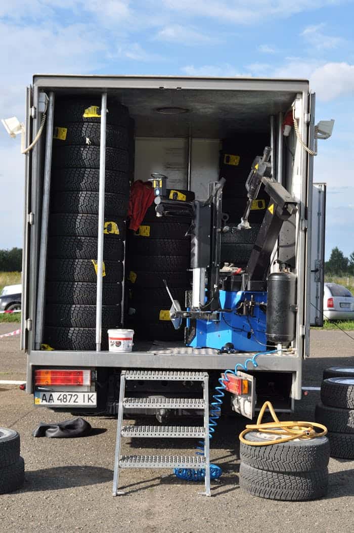 The open back of a mobile tire service truck loaded with stacked winter tires and an onboard tire changing machine