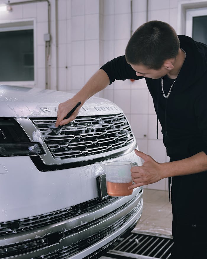 A man washing a white luxury vehicle's grill in an indoor garage, focusing on cleanliness.